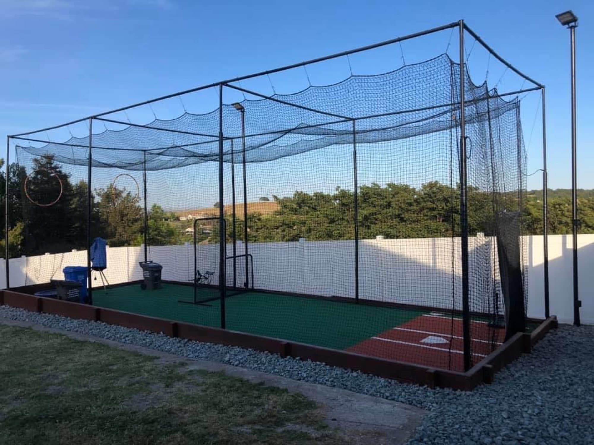 A backyard batting cage with turf, an L-screen and a pitching machine