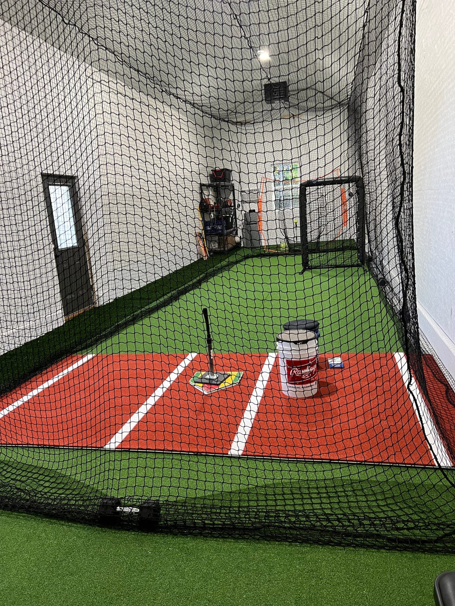 Clean netted cage with green turf, red hitting mat, tee and bucket