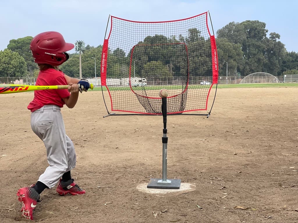 Young hitter practicing off a batting tee into a PowerNet.