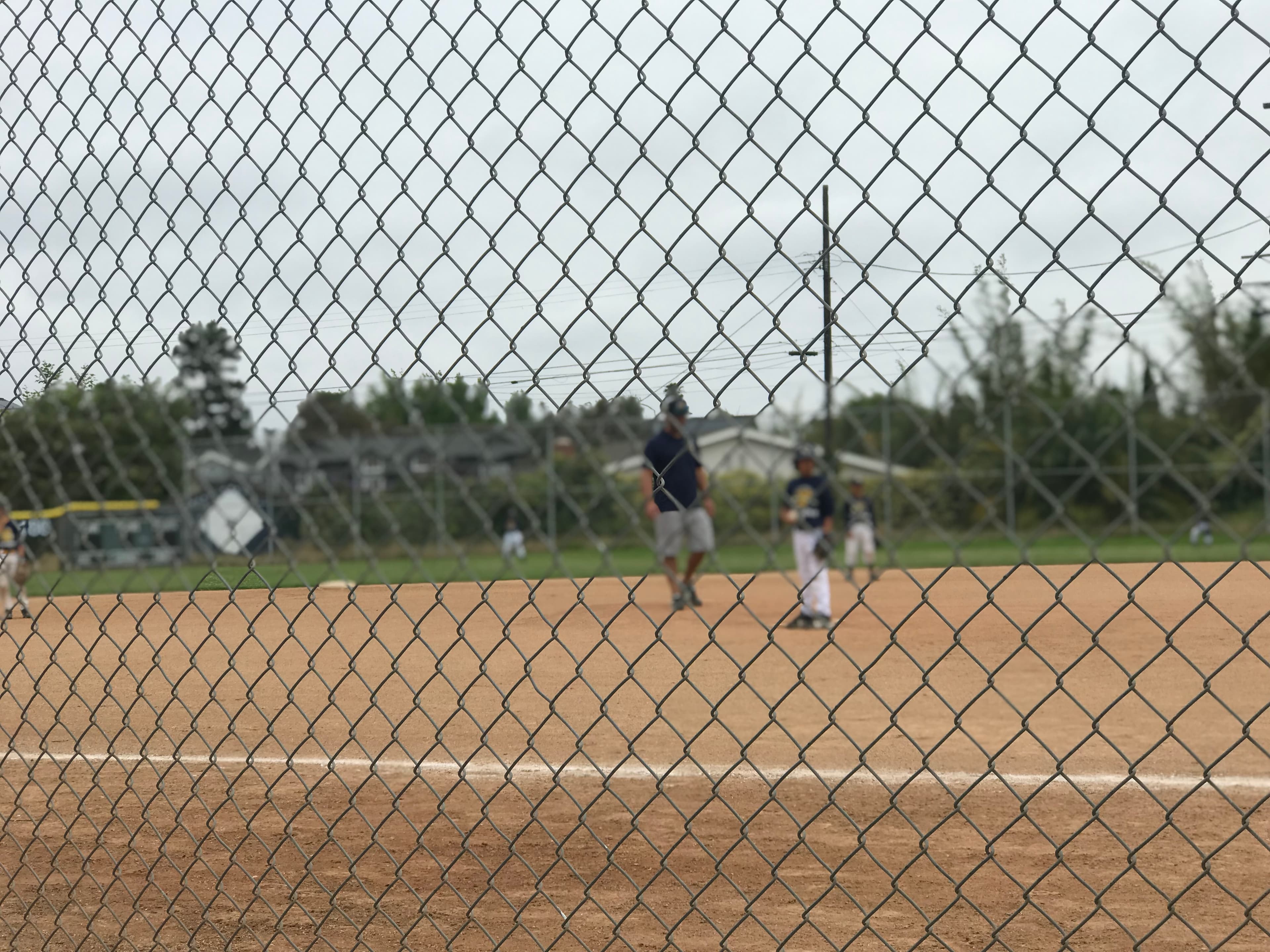 A Little League game seen through the backstop fence